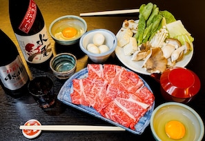 Una mesa con diversos alimentos, como una botella de sake, huevos, verduras y carne.