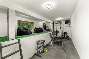 A home gym with a pull-up bar, bench press, dumbbells, kettlebells, and a TV screen displaying 'NETFLIX'.