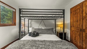 Un lit superposé avec un baldaquin, une armoire en bois et une fenêtre donnant sur les arbres.