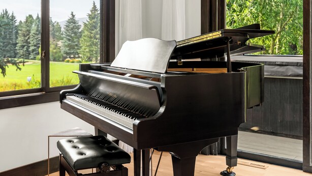 Un piano à queue dans une pièce dotée de grandes fenêtres donnant sur un paysage verdoyant.