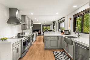 A modern kitchen with grey cabinetry, stainless steel appliances, and a large window providing a view of greenery.