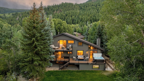 A two-story cabin with a deck, surrounded by dense forest.