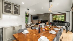 Une salle à manger spacieuse, avec une grande table en bois dressée pour le repas, un piano et une grande fenêtre offrant une vue sur l’extérieur.