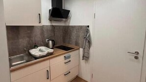 Eine kleine Küche mit weißen Schränken, einer Holzarbeitsplatte, einem Spülbecken und einem Herd.