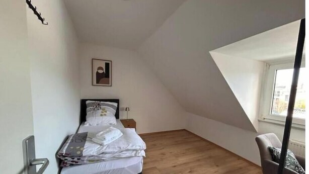 Ein Schlafzimmer mit einem Bett, einem Sessel, einem Bild an der Wand und einem Fenster.