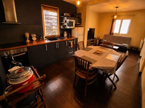 A compact kitchen with a stove, oven, microwave, and a dining area with a table and chairs. - Apartment, 2 Bedrooms for 3–4 Guests, Sauna & Ground-Floor Hot Tub (Le Tampon)