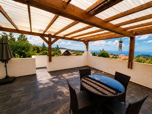 Eine überdachte Terrasse mit Tisch und Stühlen, Blick auf die Landschaft und eine Pergola.