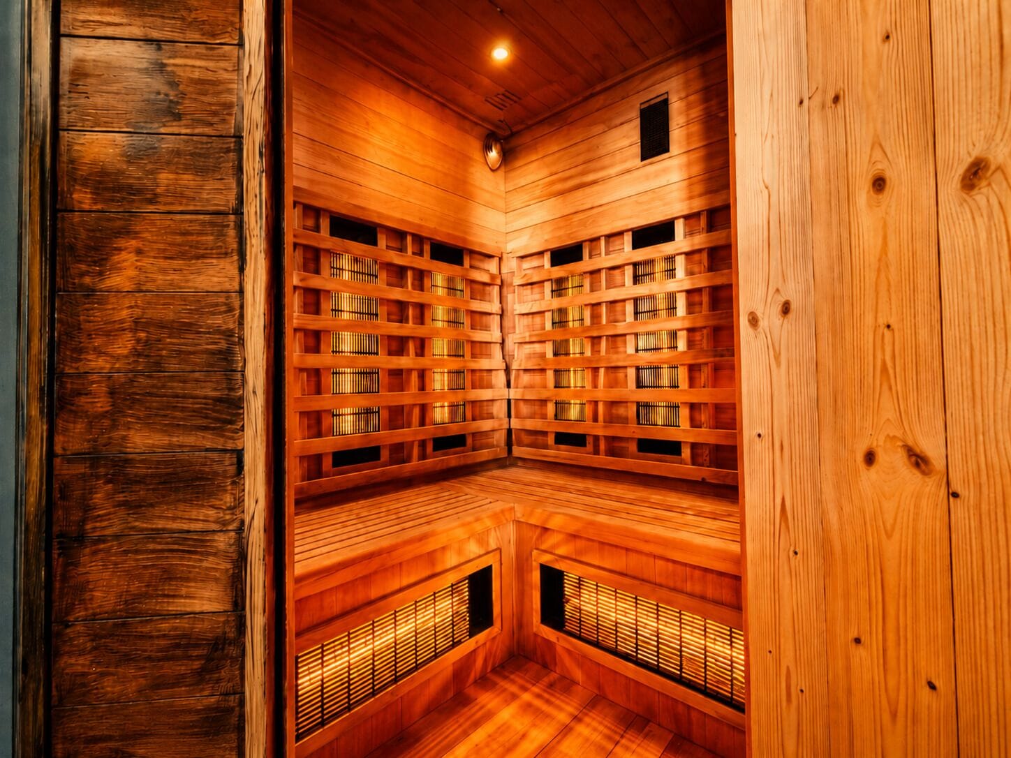 A sauna with wooden walls and benches, a ceiling light, and ventilation slats.