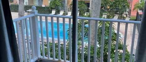 Ein Balkon mit Blick auf ein Schwimmbecken, Palmen und farbenfrohe Wohngebäude.