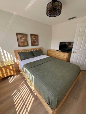 Ein Schlafzimmer mit einem Bett, einem Nachttisch aus Holz, einer Kommode, einem Fernseher und zwei gerahmten Bildern an der Wand.
