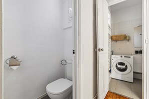 Ein Badezimmer mit Toilette, einem Papierhandtuchhalter und einer Waschmaschine im angrenzenden Raum.