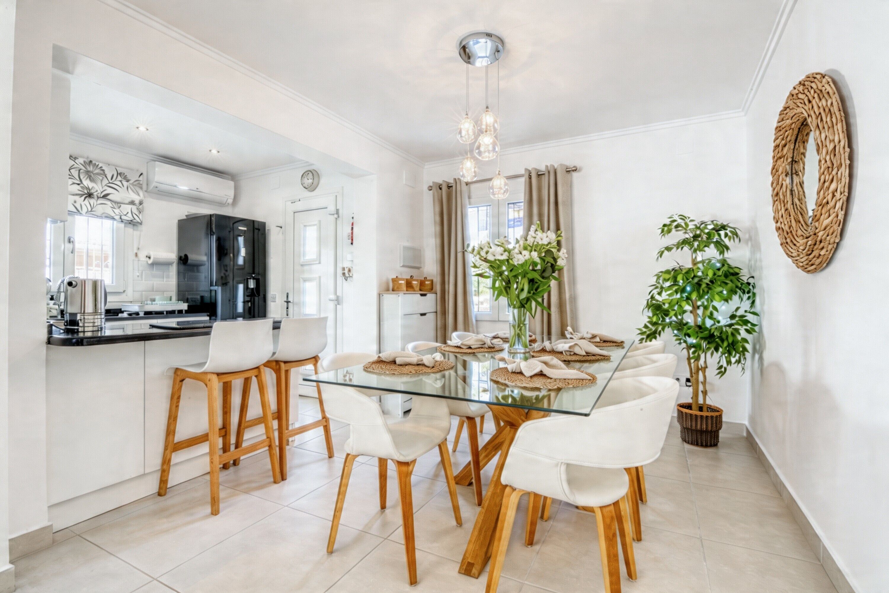 Une cuisine moderne avec une table à manger en verre, des chaises en bois et un luminaire suspendu.