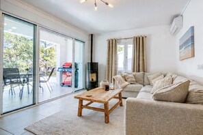 Ein Wohnzimmer mit einer Couch, einem Couchtisch und einem Kamin. Eine Glastür öffnet sich zu einem Außenbereich mit einem Grill.