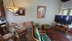 Een woonkamer met rieten meubels, een glazen eettafel, een televisie en kunstwerken aan de wanden.