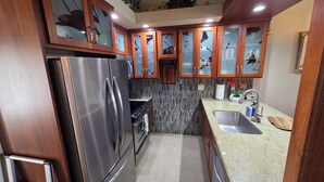 A kitchen with wooden cabinets, a stainless steel refrigerator, a tiled backsplash, and a granite countertop.