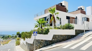 Een modern gebouw met een voetgangersoversteekplaats bord, een stenen steunmuur en uitzicht op zee.