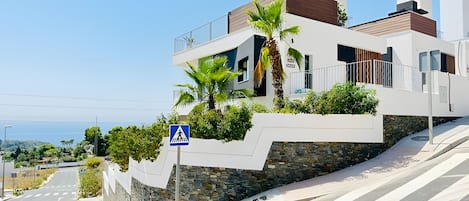 Un edificio moderno con una señal de paso para peatones, un muro de piedra y vista al mar.