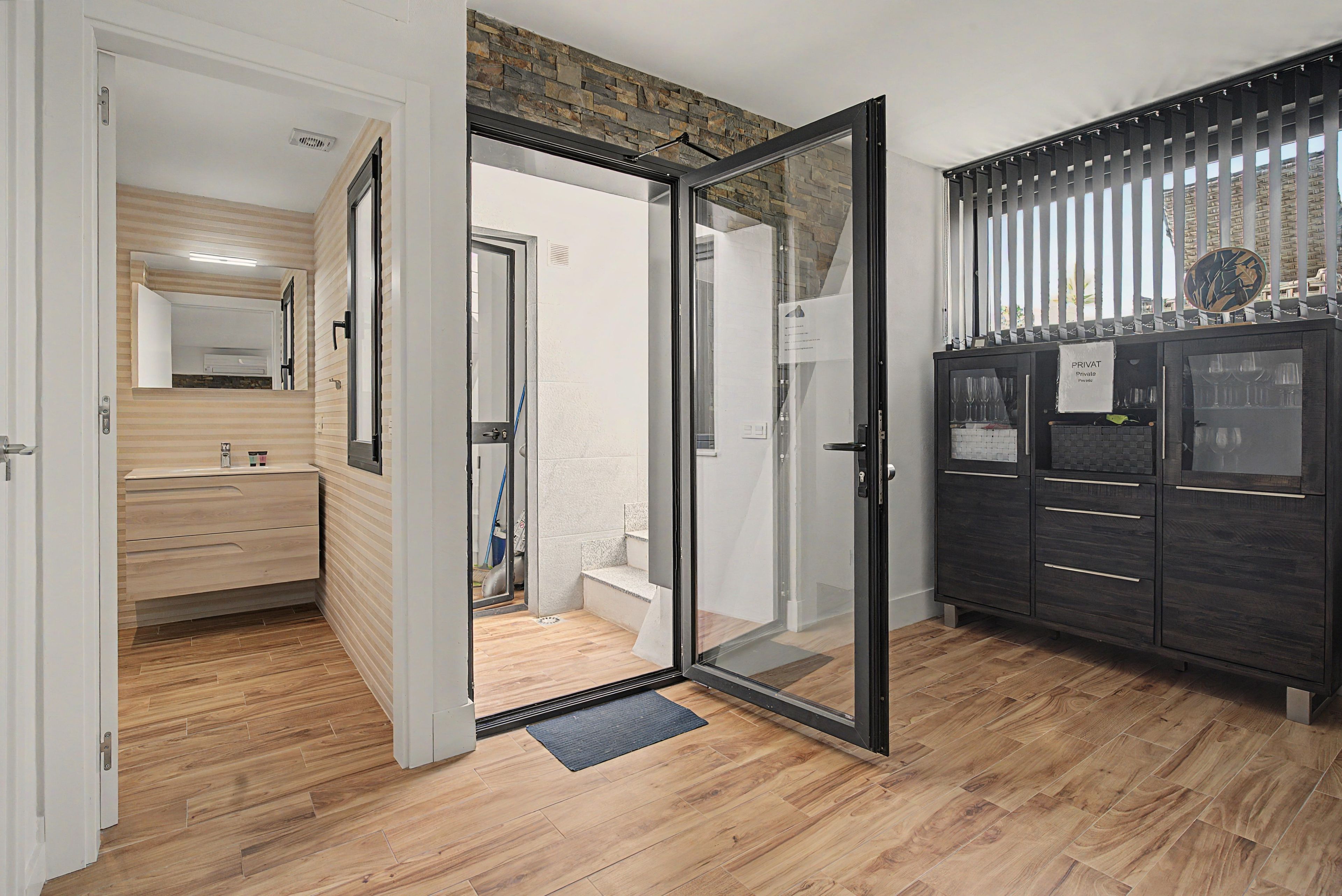 Une chambre d’hôtel avec un plancher en bois, une porte en verre donnant sur la salle de bain, un mini-bar et une vue sur l’extérieur.