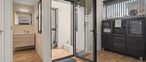 Une chambre d’hôtel avec un plancher en bois, une porte en verre donnant sur la salle de bain, un mini-bar et une vue sur l’extérieur.