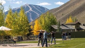 An outdoor area with a grassy field, picnic tables, and a mountain backdrop.