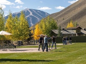 An outdoor area with a grassy field, picnic tables, and a mountain backdrop.