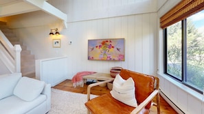 A cozy living room with a white sofa, a wooden chair with a cushion, a painting on the wall, and a staircase. - Creekside Condo 1304 - Newly Remodeled Sun Valley Loft (Sun Valley)