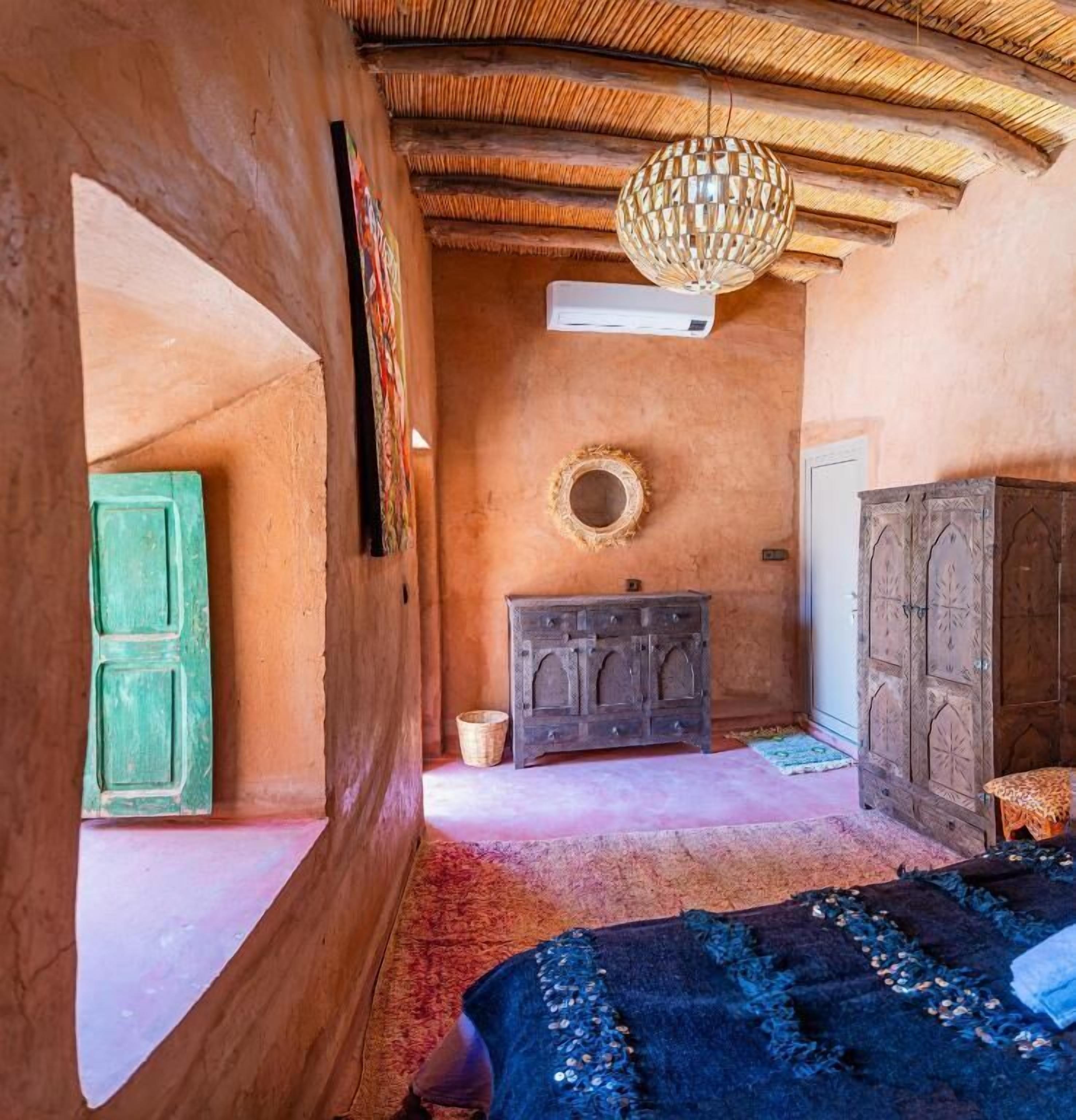 Una habitación rústica con techo de madera, una cama con colcha estampada, un aparador y una puerta verde.