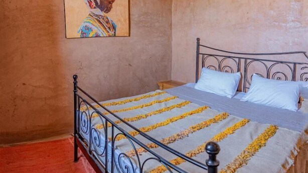 A bedroom with a bed, a painting on the wall, and a woven ceiling light.