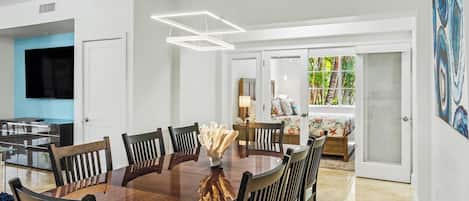 Un espace repas moderne avec une table et des chaises en bois, un élément décoratif central et une vue sur une chambre à coucher avec un lit et une fenêtre.