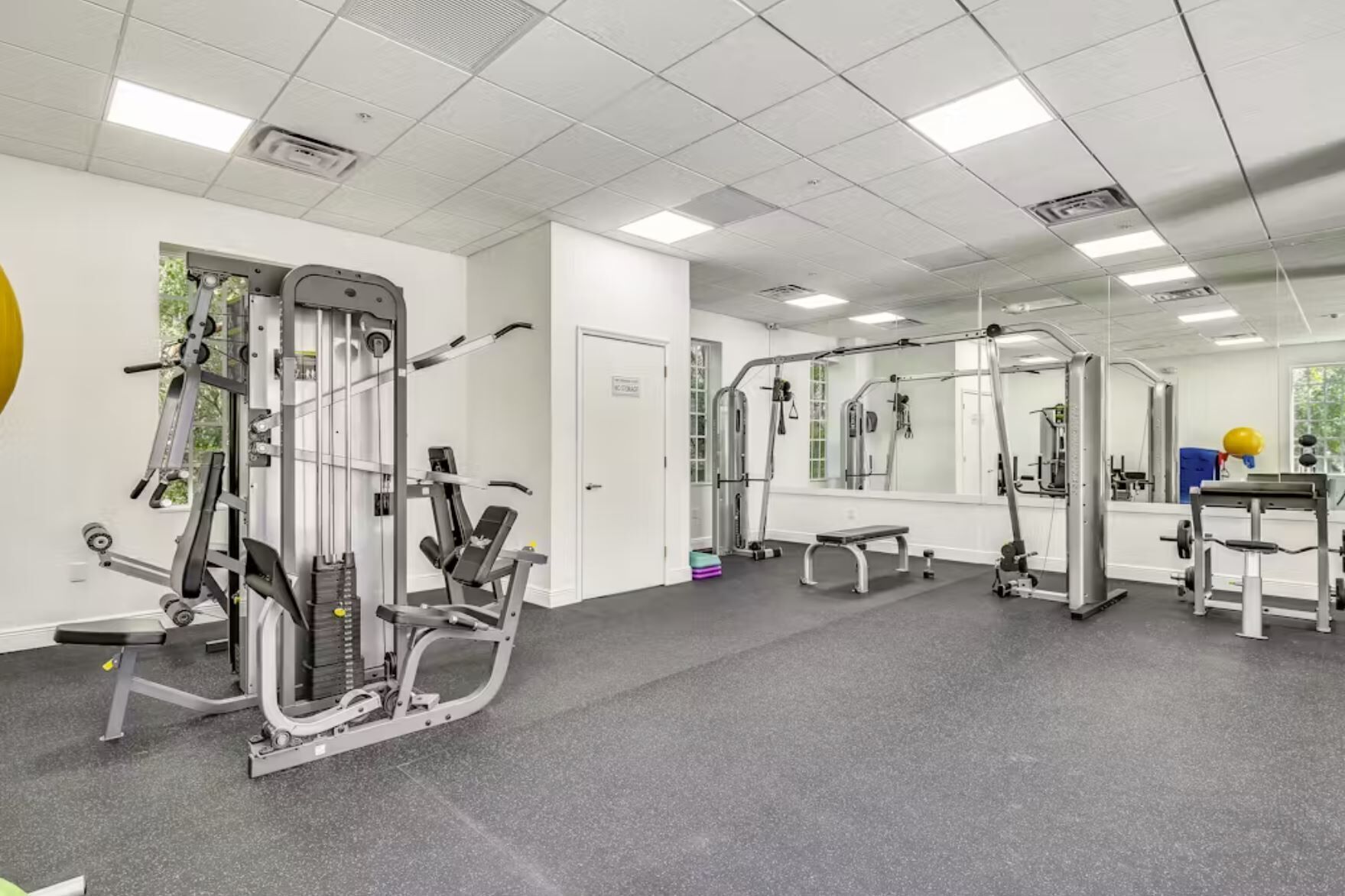 A gym with various exercise machines, a bench, and a large mirror.