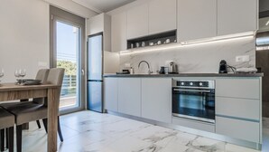 A modern kitchen with a built-in oven, a dining area with a table and chairs, and a view of the outdoors through a sliding door. - Ireon Luxury Suites 1 by RentalsPro - Nea Plagia Halkidiki (Nea Plagia)