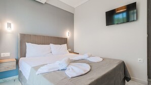 A hotel room with a bed, a TV mounted on the wall, and a towel on the bed. - Ireon Luxury Suites 1 by RentalsPro - Nea Plagia Halkidiki (Nea Plagia)