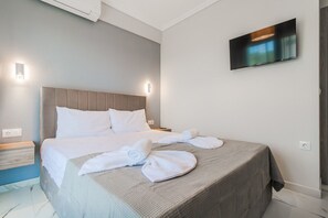 A hotel room with a bed, a TV mounted on the wall, and a towel on the bed. - Ireon Luxury Suites 1 by RentalsPro - Nea Plagia Halkidiki (Nea Plagia)