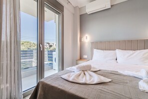 A hotel room with a bed, a nightstand, a wall-mounted air conditioner, and a sliding glass door leading to an outdoor area. - Ireon Luxury Suites 1 by RentalsPro - Nea Plagia Halkidiki (Nea Plagia)