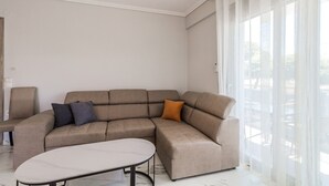 A modern living room with a sectional sofa, a small table, and sheer curtains. - Ireon Luxury Suites 1 by RentalsPro - Nea Plagia Halkidiki (Nea Plagia)