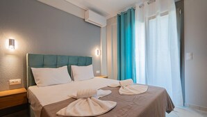 A hotel room with a bed, a nightstand, a wall-mounted air conditioner, and a window with curtains. - Ireon Luxury Suites 2 by RentalsPro - Nea Plagia Halkidiki (Nea Plagia)