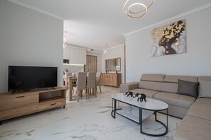 Ein modernes Wohnzimmer mit Flachbildfernseher, einer Couch, einem Couchtisch und einem Essbereich mit Stühlen und einem Holzschrank.