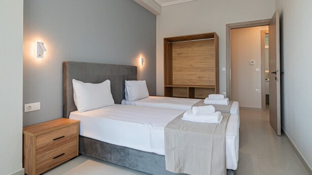 A modern hotel room with two beds, a wooden headboard, bedside tables, and a wardrobe. - Ireon Luxury Suites 4 by RentalsPro - Nea Plagia Halkidiki (Nea Plagia)