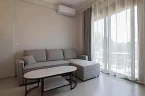 Ein modernes Wohnzimmer mit einem grauen Sofa, einem kleinen Tisch und einem großen Fenster mit transparenten Vorhängen.