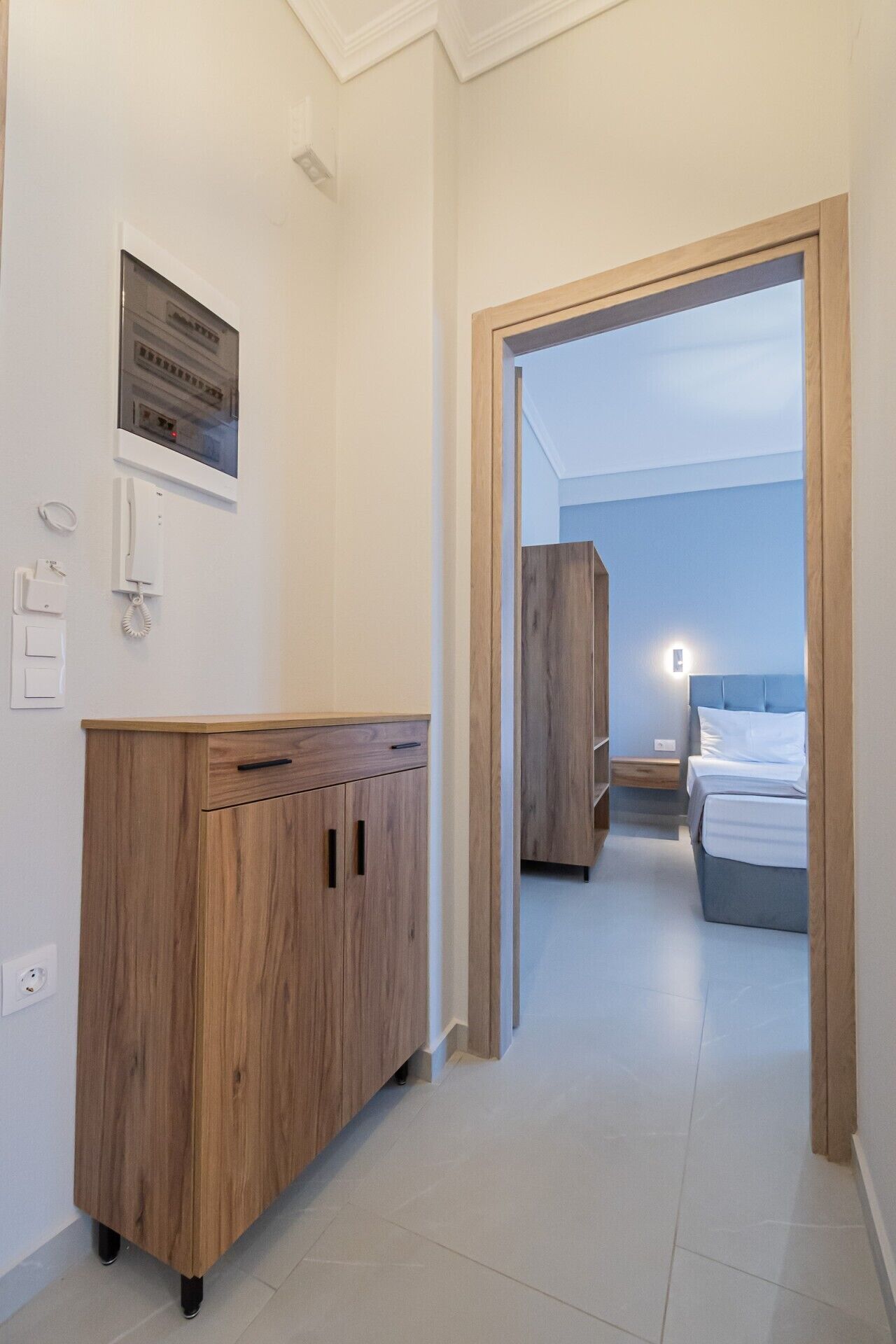 A hotel room with a wooden wardrobe, a bed, and a nightstand.