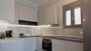 A modern kitchen with white cabinetry, a built-in oven, and a window above the sink. - Ireon Luxury Suites 4 by RentalsPro - Nea Plagia Halkidiki (Nea Plagia)