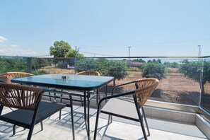 A terrace with a table and chairs, overlooking a vineyard.