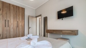 A hotel room with a bed, a TV mounted on the wall, a wooden wardrobe, and a mirror. - Ireon Luxury Suites 3 by RentalsPro - Nea Plagia Halkidiki (Nea Plagia)