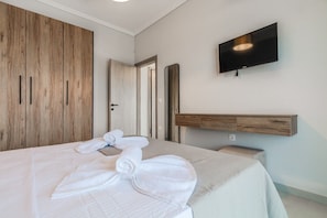 Ein Hotelzimmer mit Bett, Wandfernseher, Holzschrank und Spiegel.