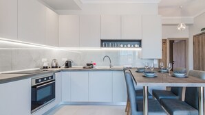 A modern kitchen with a built-in oven, a sink, and a dining area with a table set for two. - Ireon Luxury Suites 3 by RentalsPro - Nea Plagia Halkidiki (Nea Plagia)