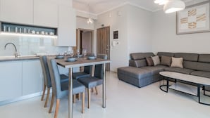 A modern kitchen with a dining area, a grey sofa, and pendant lights. - Ireon Luxury Suites 3 by RentalsPro - Nea Plagia Halkidiki (Nea Plagia)