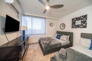 A hotel room with a bed, a TV, a ceiling fan, a window, and a wall clock. - 3-bedroom apartment in the best location in Condado (San Juan)