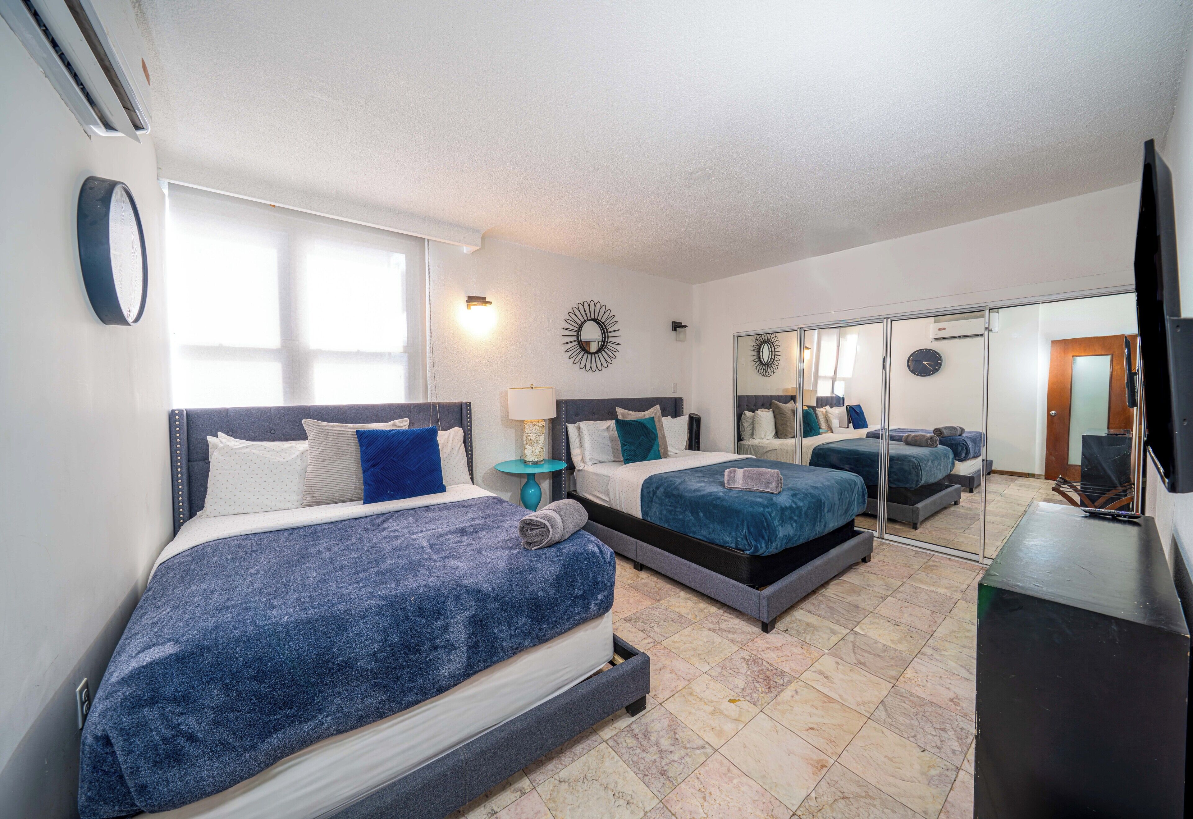 Une chambre d’hôtel avec deux lits, une télévision, un miroir et une horloge au mur.