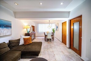A spacious living area with a brown sofa, a dining table, and a kitchen area in the background. - 3-bedroom apartment in the best location in Condado (San Juan)