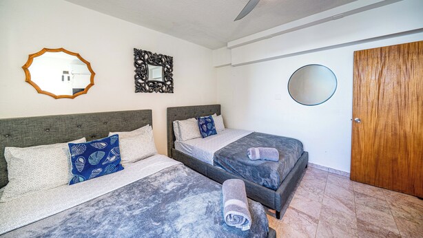 Quarto de hotel com duas camas, um ventilador de teto, uma porta de madeira e um espelho na parede.